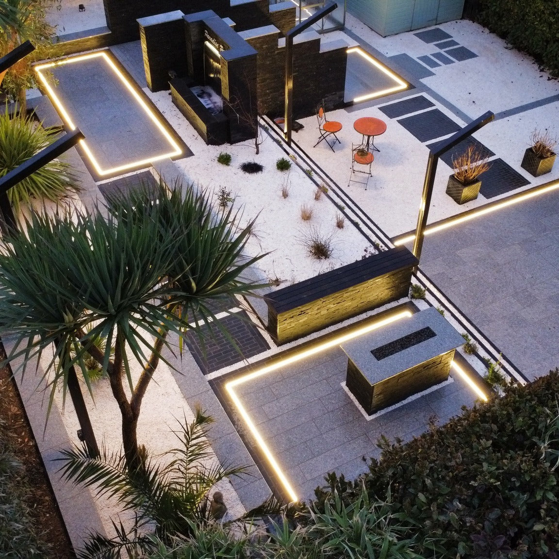 Contemporary garden featuring a black RAL 9005 ANCO steel retaining wall with tropical palm planting. Steel edging, garden borders and raised beds