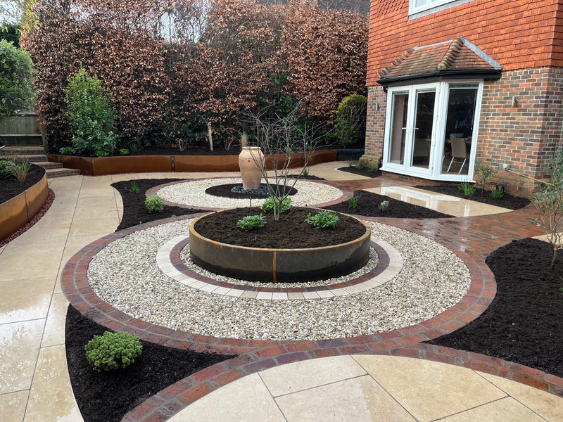 Modern landscaped garden with Corten Contour Raised bed steel garden edging, circular raised beds, gravel planting beds and porcelain paving in a contemporary UK garden. Weathering steel, rust patina, garden edging and planting borders.