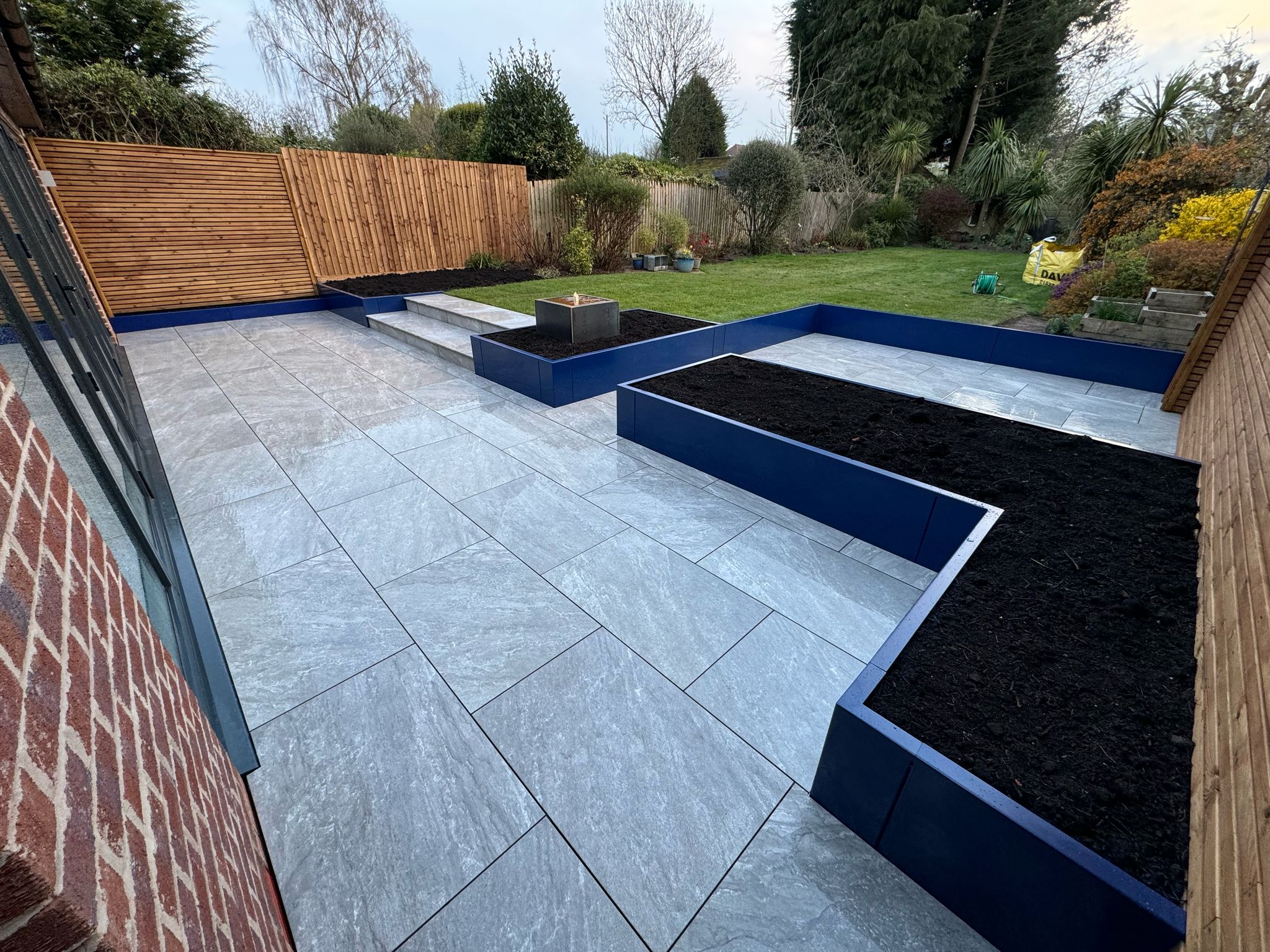 Cobalt blue powder-coated steel garden planters in a contemporary landscaped garden.
