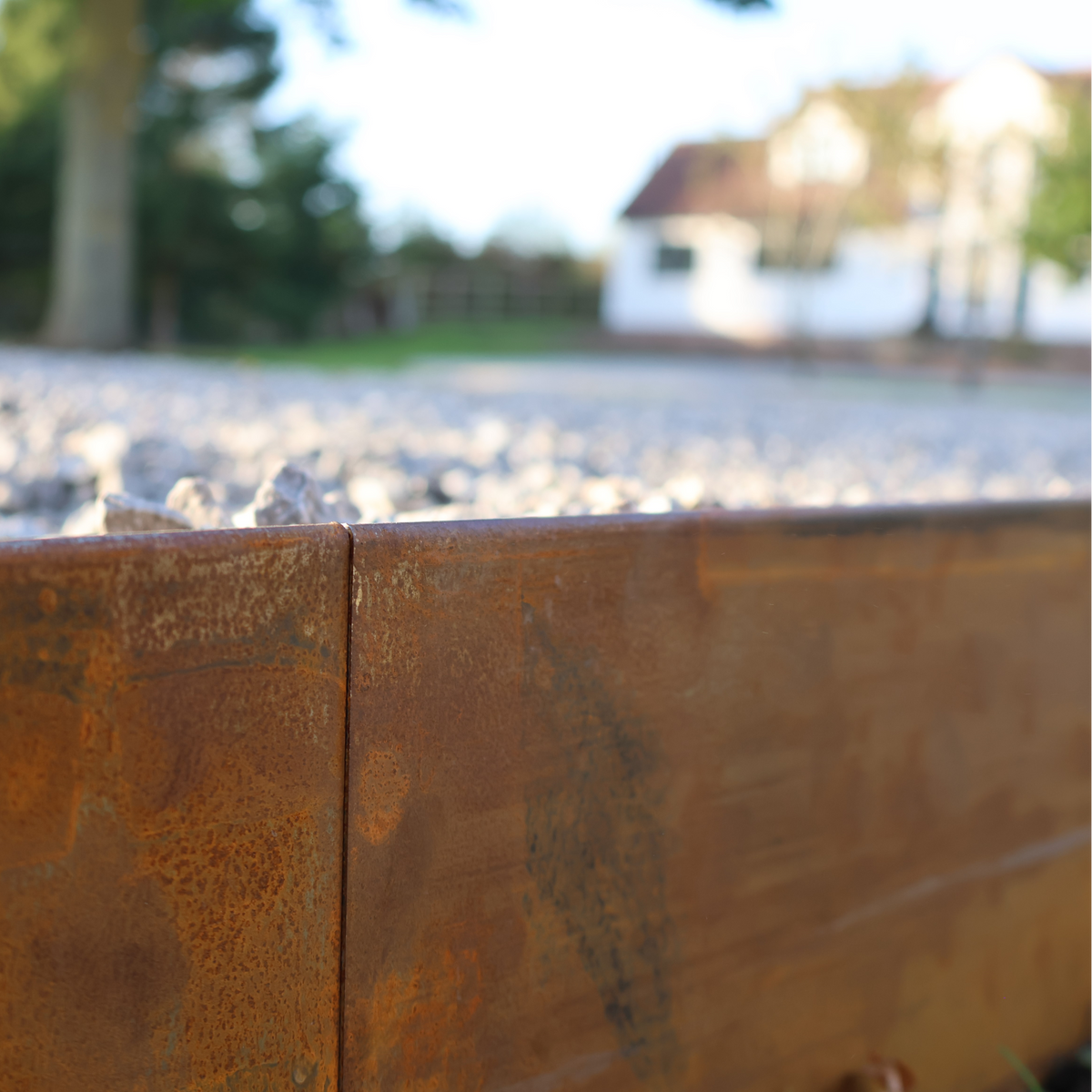 Groundline - Edge height 150mm GEO. Showing low edge roll top and seamless joins. High Corten Steel Garden Edging, creating boundary between soil, planting and gravel path. Lawn edge, garden border, flower beds, driveway raised edging. Metal, weathering steel, or powder coated steel.  Garden walkway, path and paving. Planter edge and retaining wall. Patio edge and garden walls.