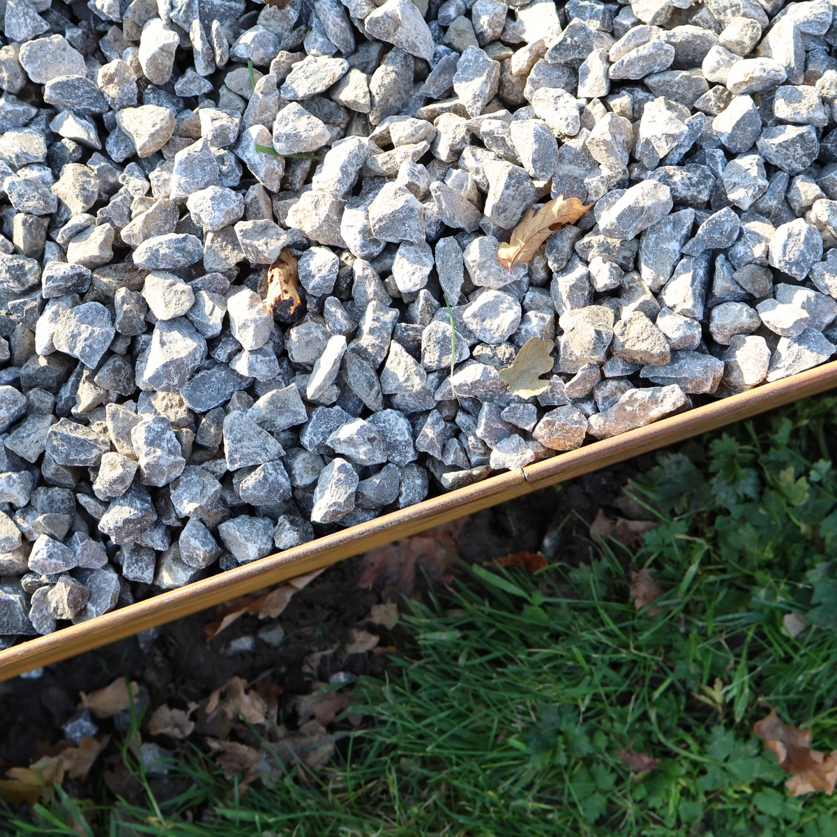 75mm High Corten Steel Garden Edging, creating boundary between lawnand gravel path. Lawn edge, garden border, flower beds, raised edging. Metal, weathering steel, mild steel or powder coated steel.  Garden walkway, path and paving edging. Close up of roll top edge