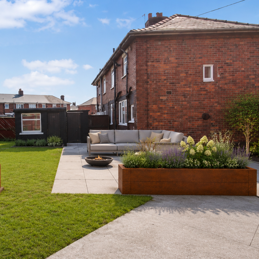 A landscaped backyard patio scene with a green lawn, brick house, paved walkway, outdoor seating, and two large rectangular wooden planter boxes with flowering shrubs under a blue sky.