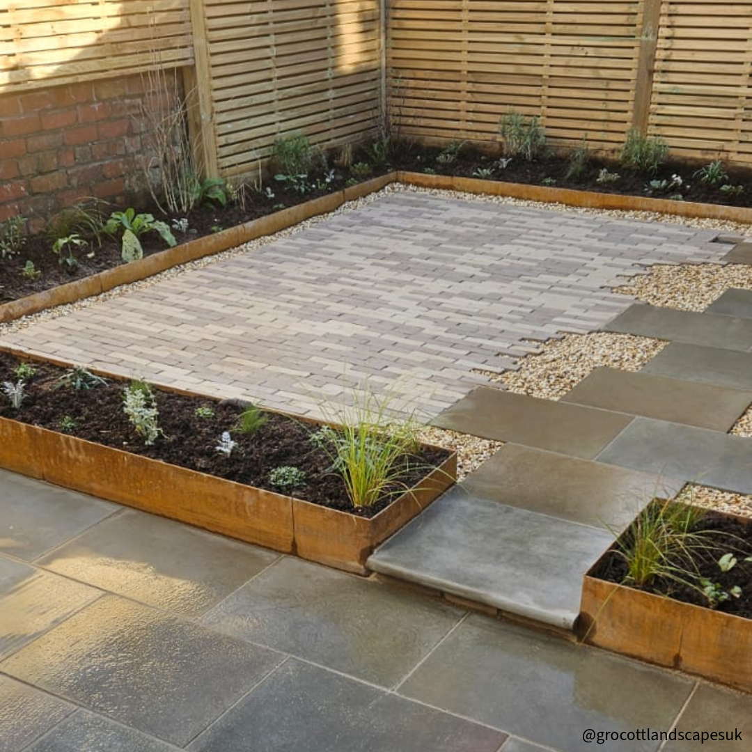 Groundline Garden Edging – 200mm High (10 Metre Pack) GEO, Showing Corten steel edging used as a garden border to create planters around patio area. High Corten Steel Garden Edging, creating boundary between soil, planting and gravel path. Lawn edge, garden border, flower beds, driveway raised edging. Metal, weathering steel, or powder coated steel.  Garden walkway, path and paving. Planter edge and retaining wall. Patio edge and garden walls.